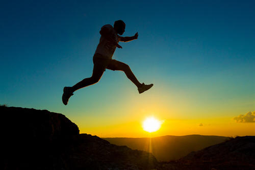 Man hiker leaping into the air over a setting sun 